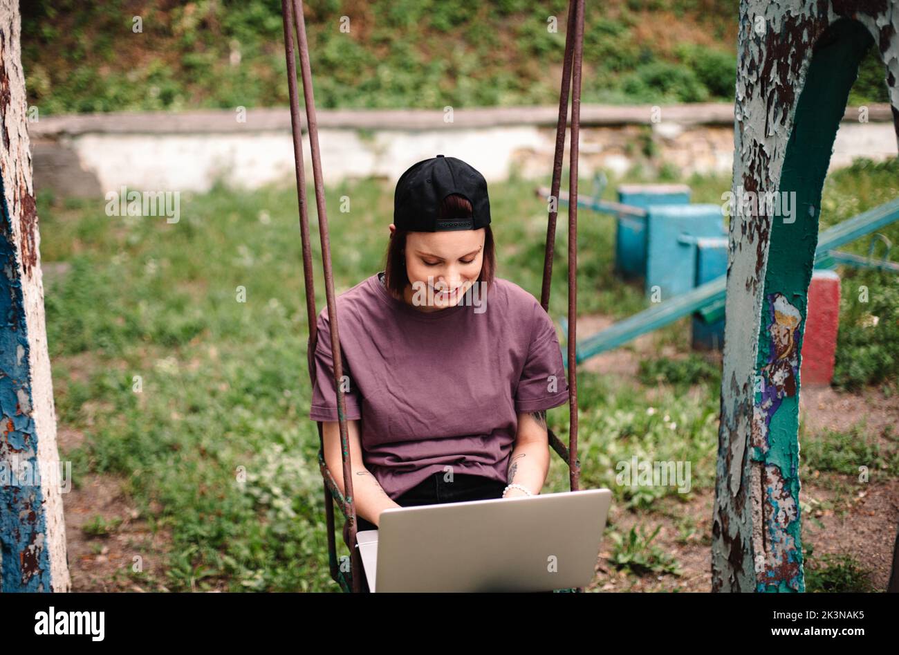 Happy young female student using laptop sitting on a swing Stock Photo