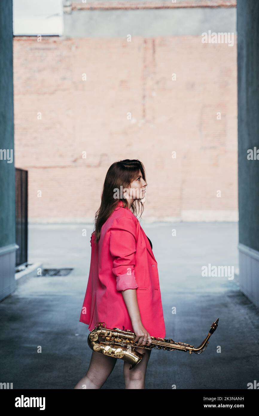 young girl in a pink jacket with a saxophone in her hand Stock Photo