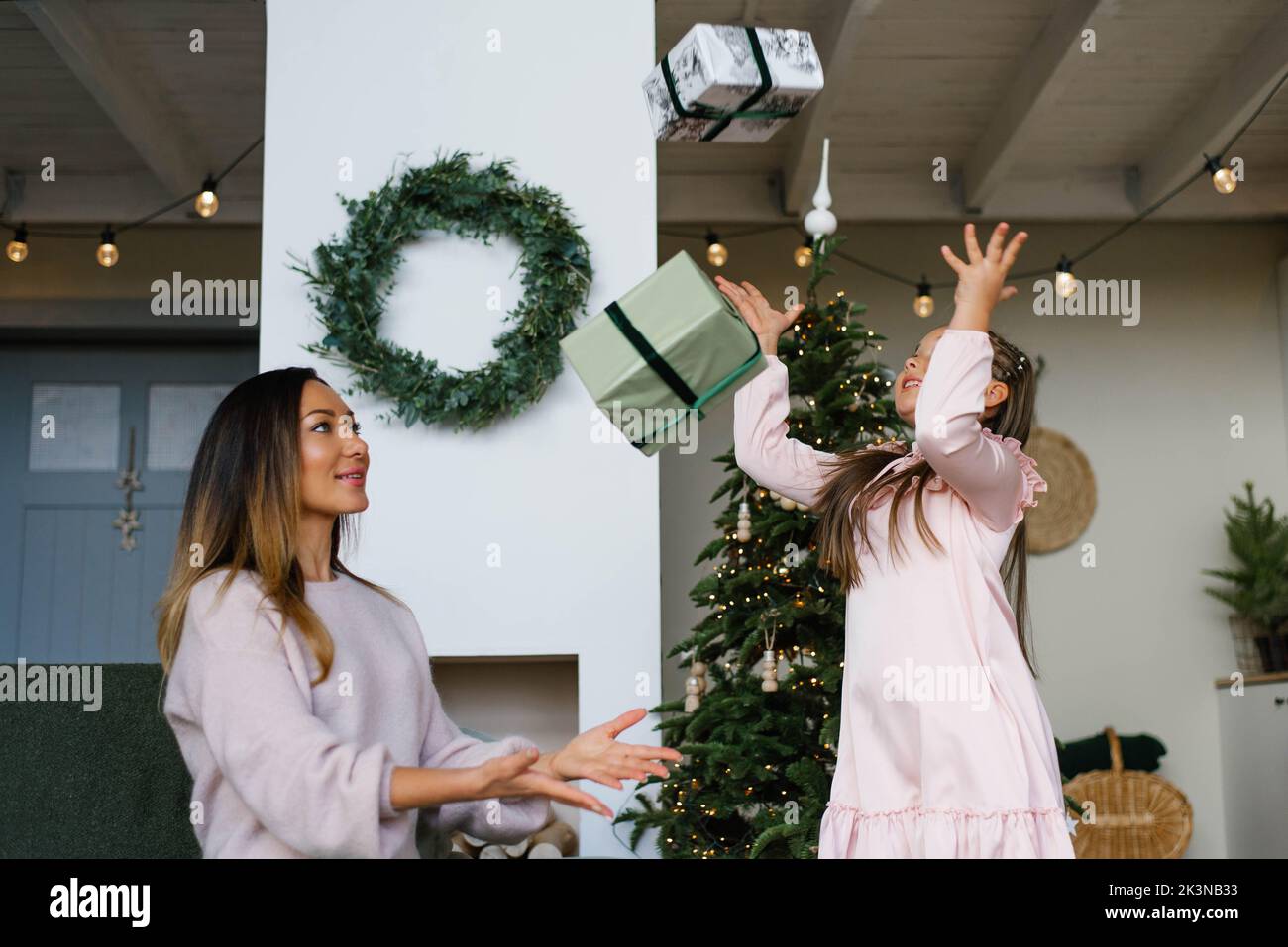 Mother and daughter celebrate at the Christmas tree, throwing up gifts Stock Photo