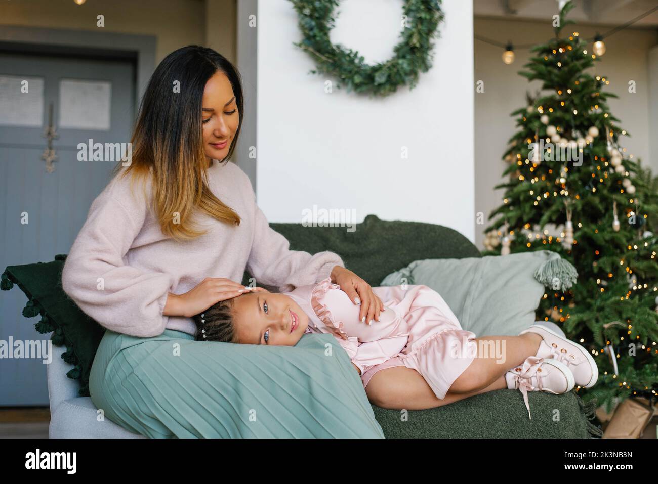 Daughter put head on mother's lap and is smiling at the Christmas tree Stock Photo