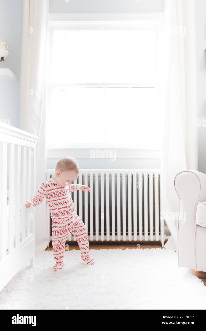 1-2 year old Caucasian toddler in Christmas pajamas walks in nursery. Stock Photo
