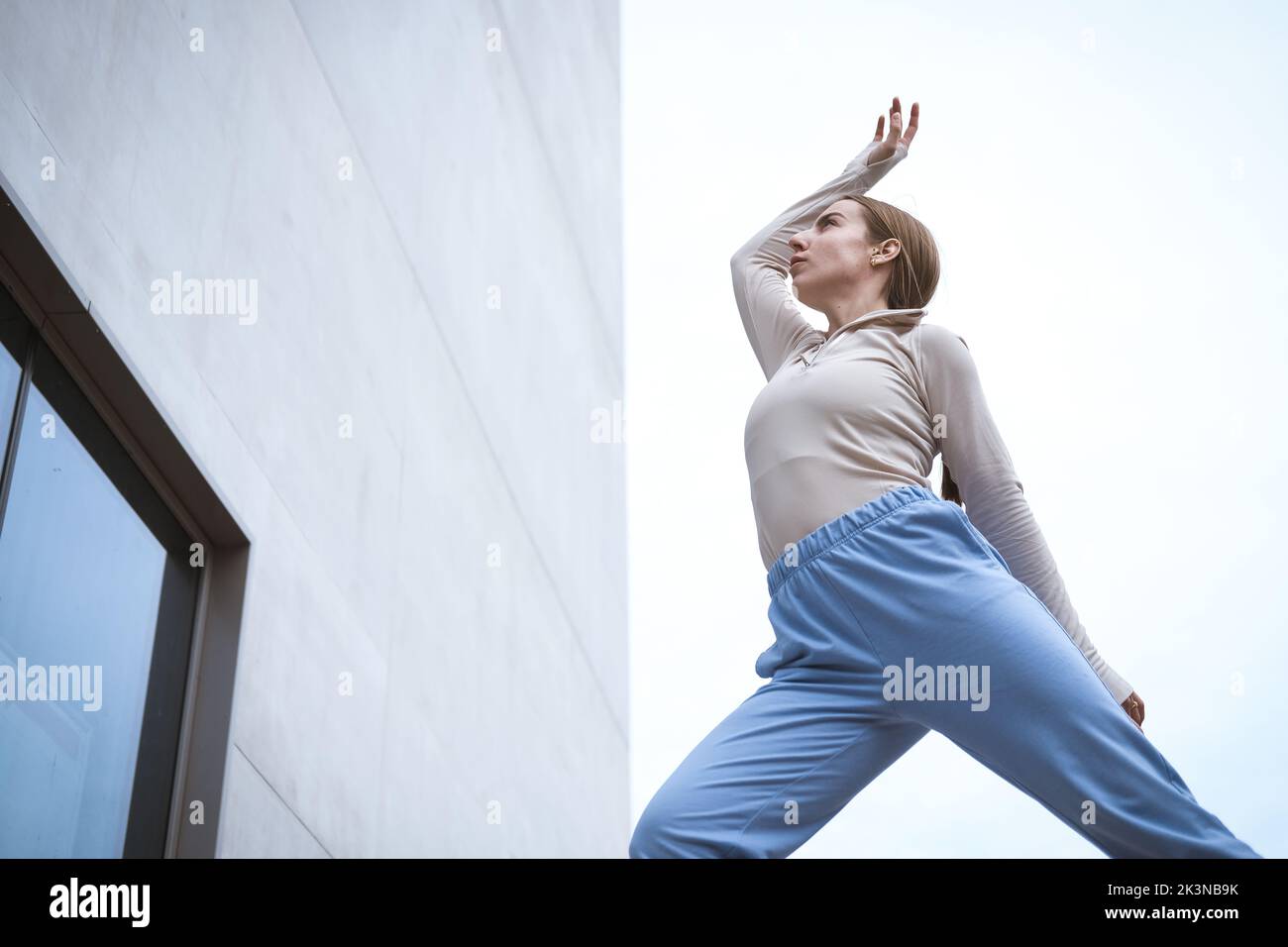 Girl in a blue pants stretching and dancing against grey wall Stock Photo
