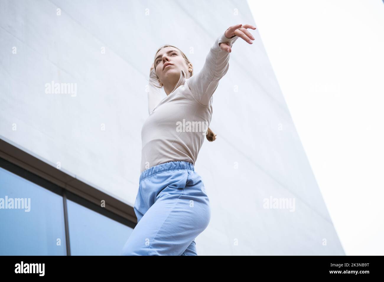 Girl in a blue pants stretching and dancing against grey wall Stock Photo