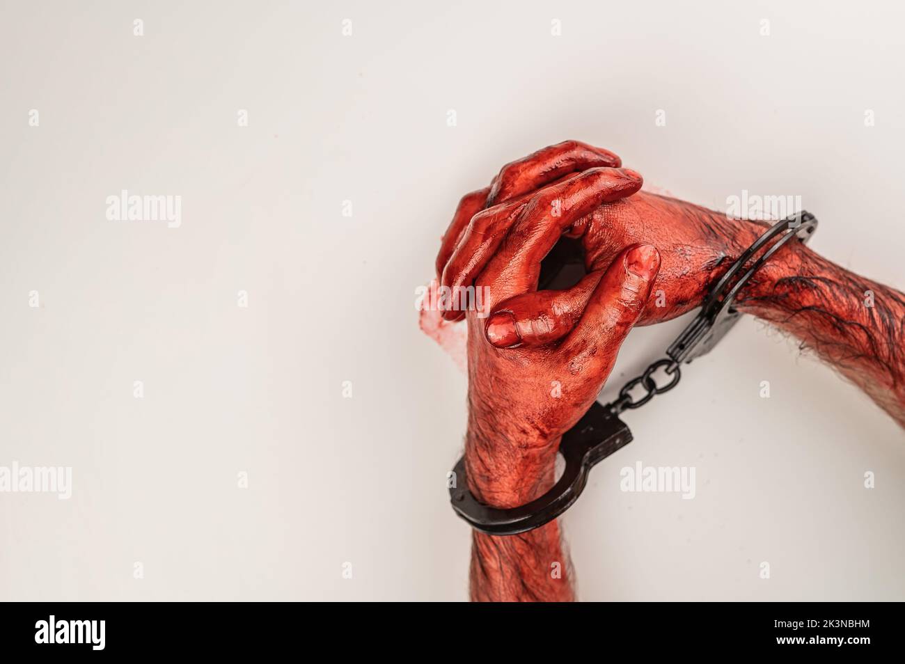 Bloodied male hands in handcuffs, folded on a white table. Stock Photo