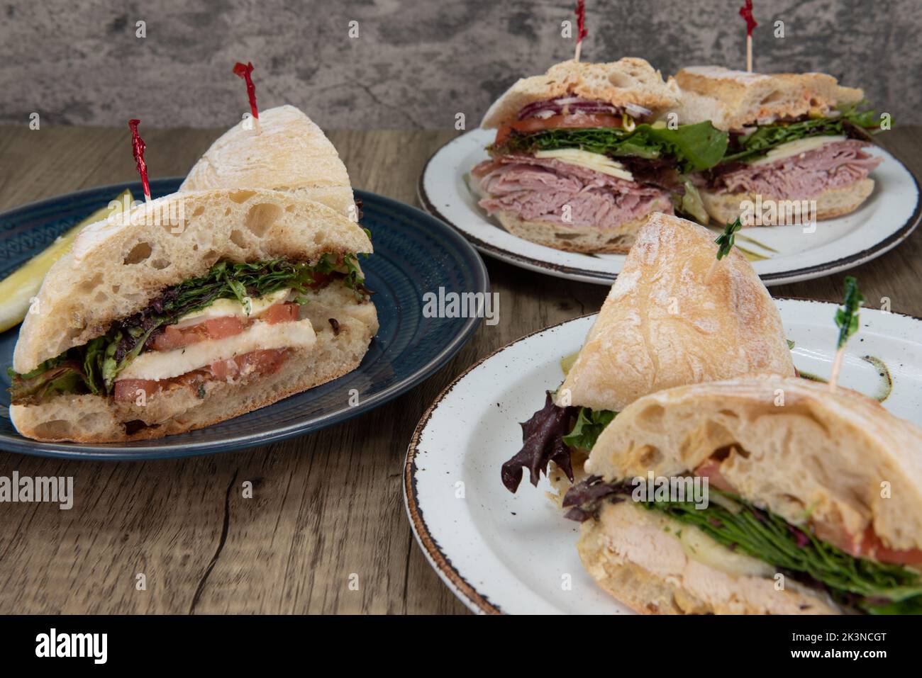 Table feast of deli sandwiches with the provolone cheese, tomato, and savoy greens sub served on a ciabatta bun featured in the middle. Stock Photo