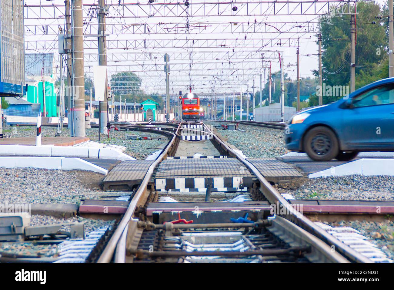 Kemerovo, Russia - September 01, 2022. A red locomotive is approaching a railway crossing which is about to be crossed by a passenger car, selective f Stock Photo
