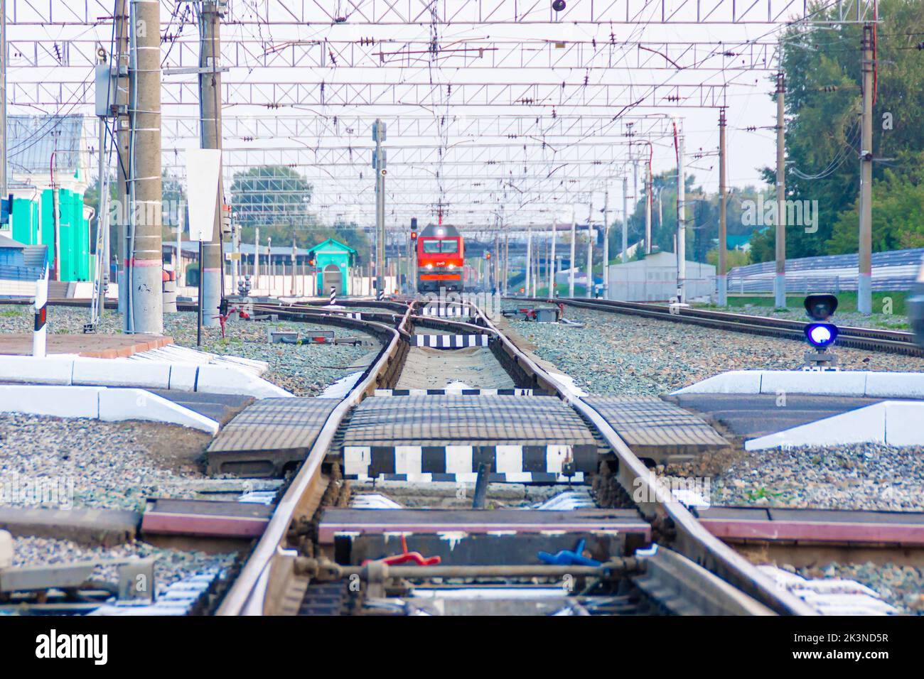 Kemerovo, Russia - September 01, 2022. Red locomotive of Russian railways is approaching the railway crossing while driving away from a small station, Stock Photo
