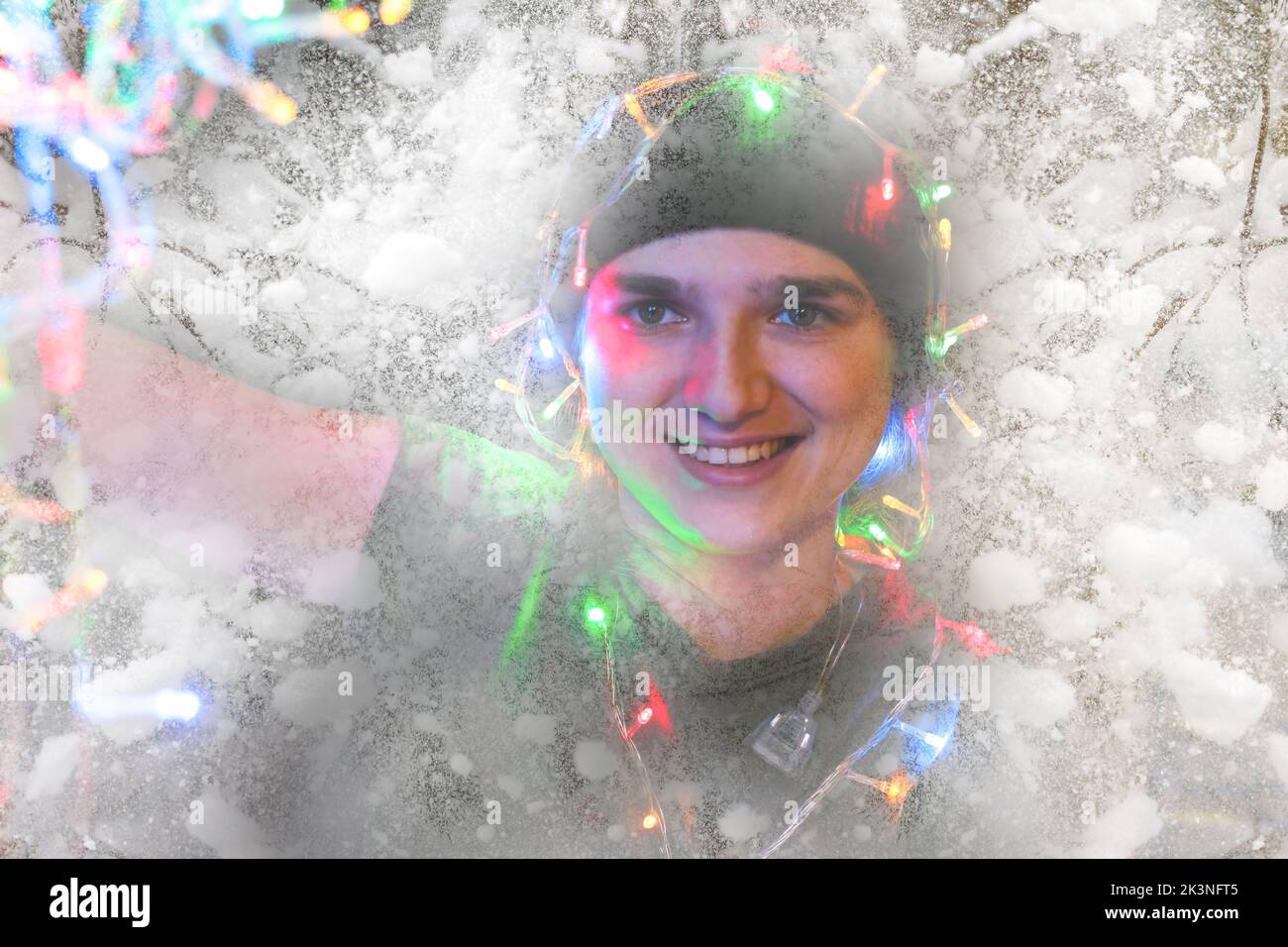 Defocus close-up portrait of a festive young woman with garland on her face and head. Hipster girl celebrates christmas. Bokeh and lights. Girl 25 yea Stock Photo