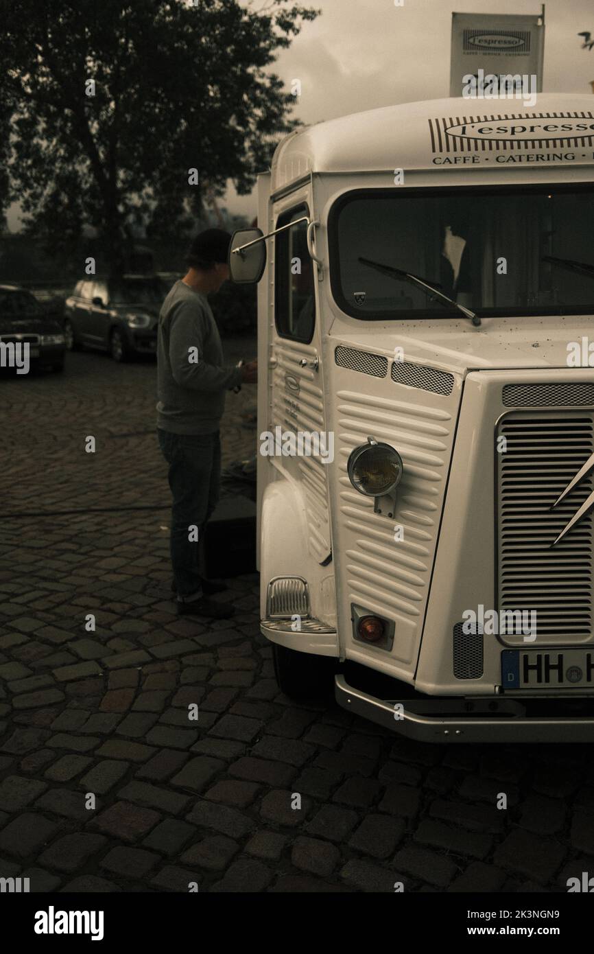 A man standing next to a vintage white truck with other cars parked in the background on a gloomy day Stock Photo