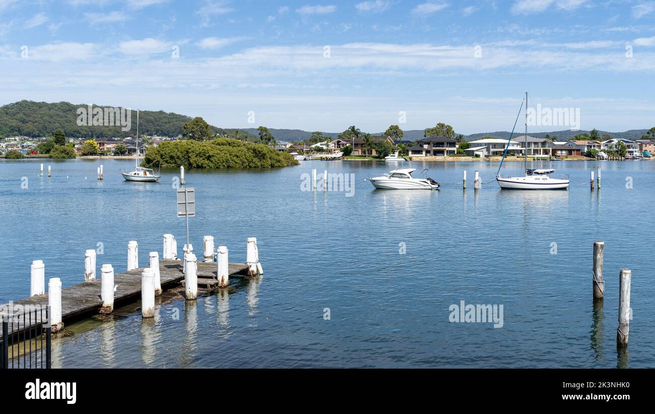 Beautiful coastal Australian scenery of small dock in lake with boats and yachts. Hill in the distance. Blue sky and blue water on sunny day. Stock Photo