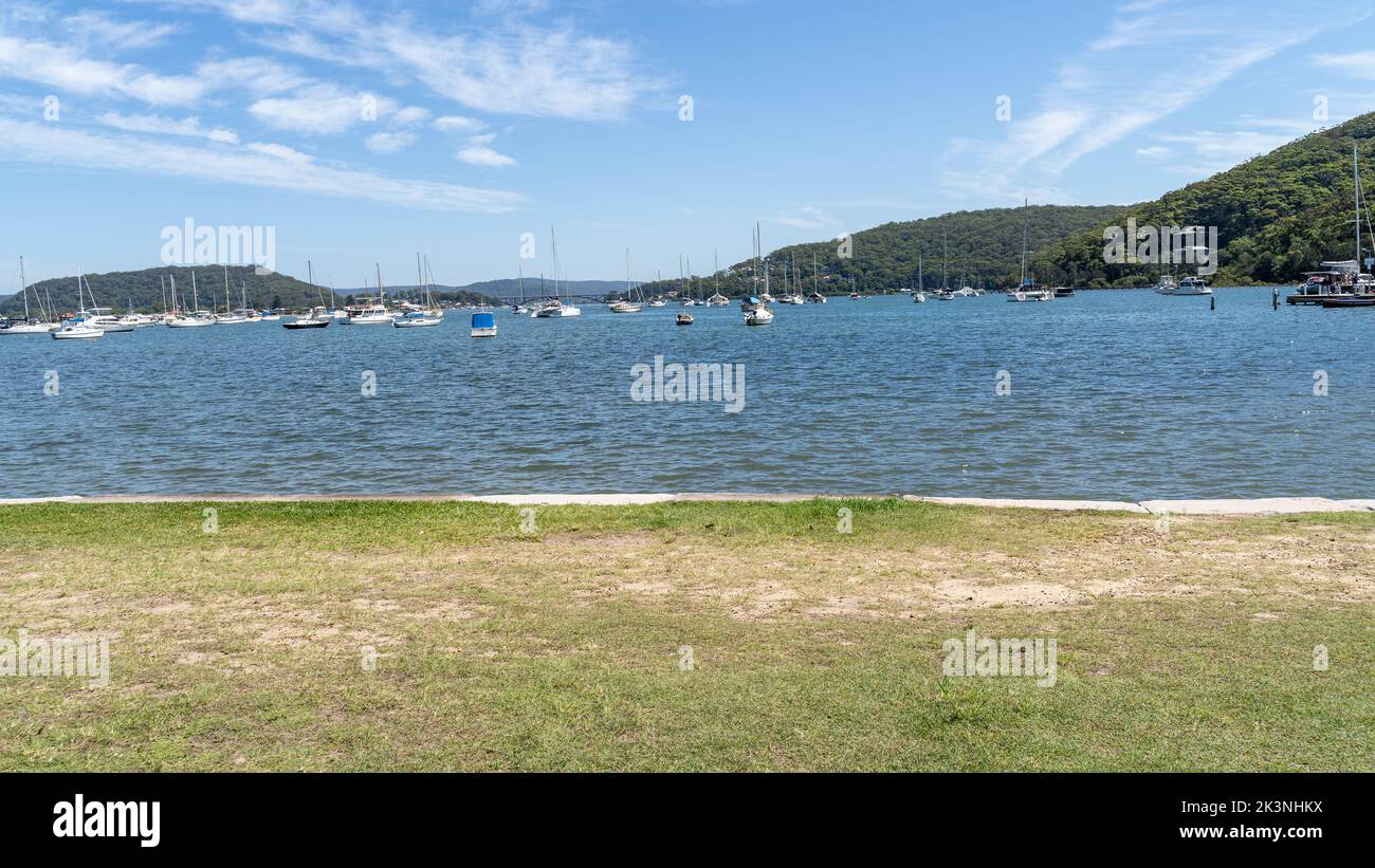 Sunny day wide Australian landscape of river bank and hills in distance. Blue summer sky and boats in water. Stock Photo