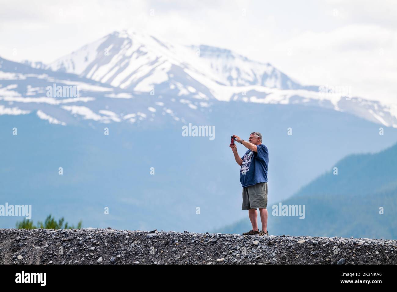 Lone male tourist taking pictures of Canadian Rocky Mountains with a mobile phone; Muncho Lake; British Columbia; Canada Stock Photo