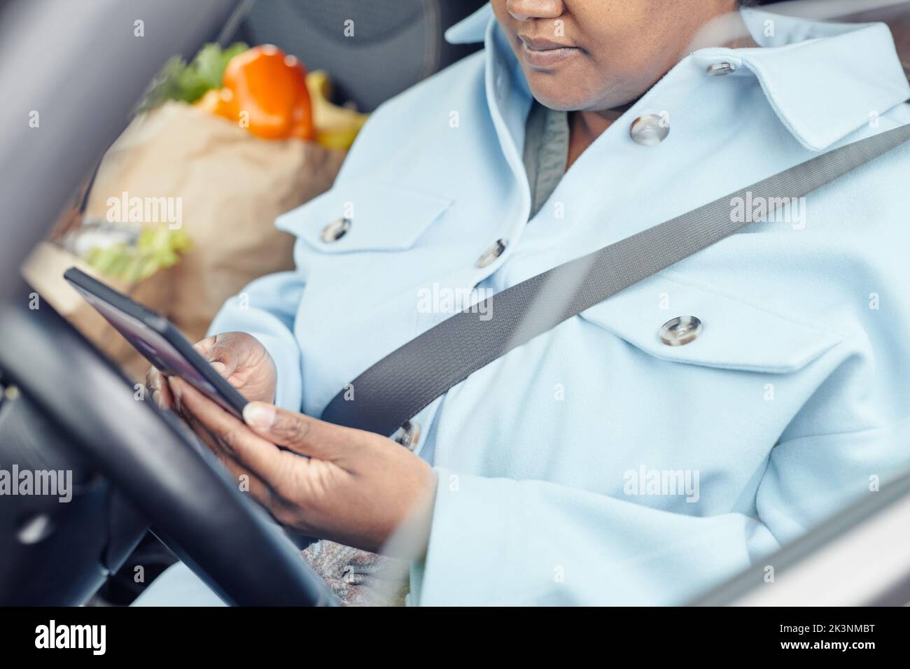 Close up of young black woman using smartphone in car with focus on safety belt Stock Photo