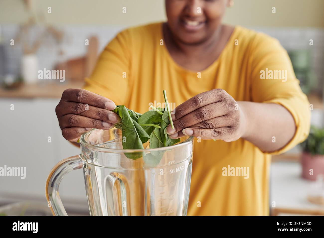 Close up of young black woman putting spinach in blender while making