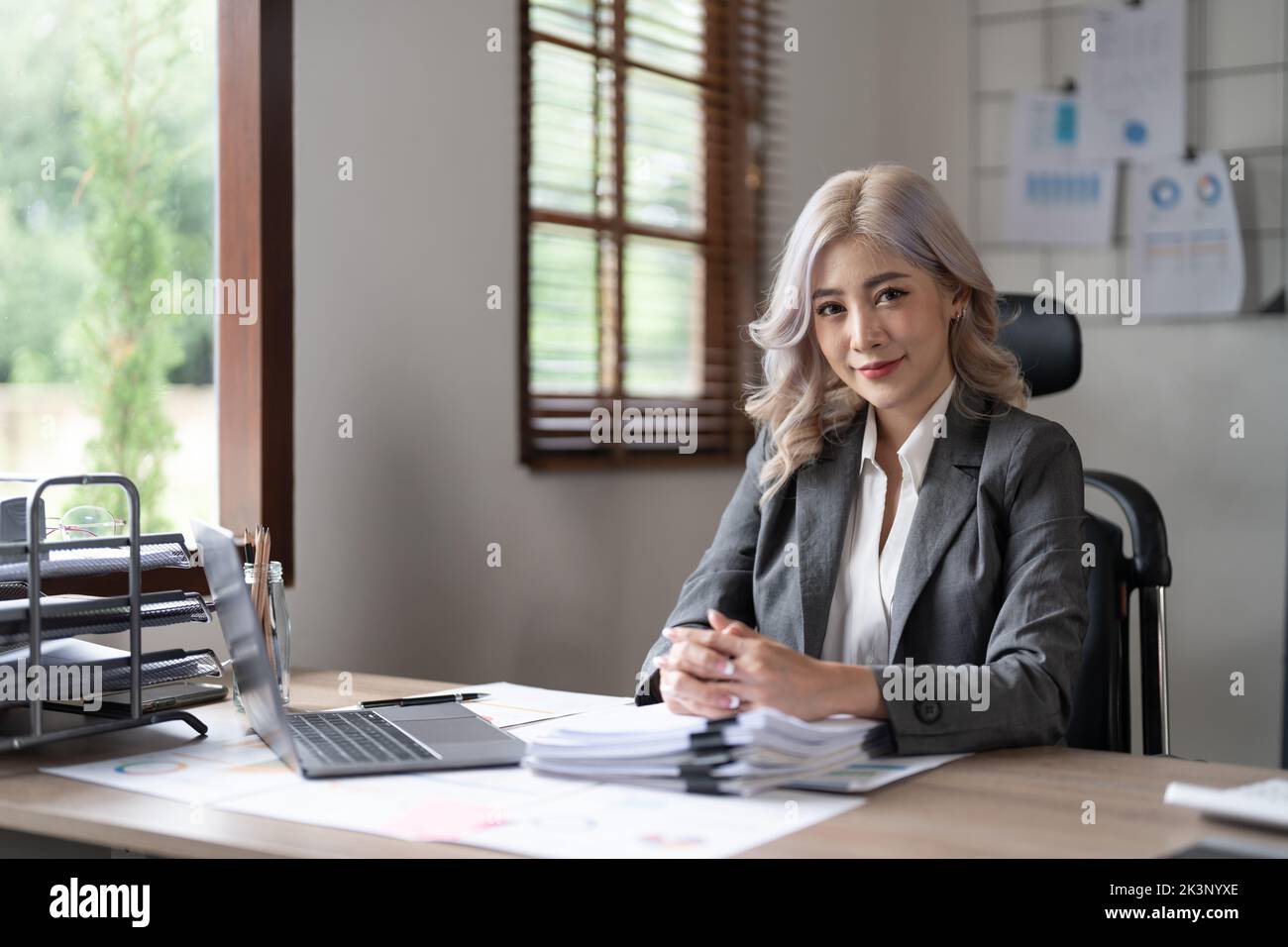 Pretty asian businesswoman smiles at the camera while sitting at her desk in front of the computer. Stock Photo