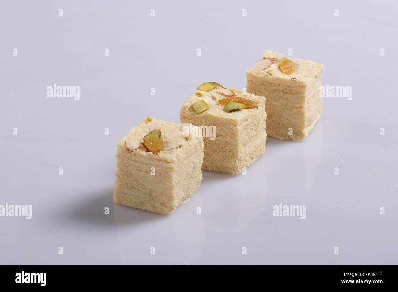 Soan Papdi is a popular Indian cube shape flakey crispy dessert. Served with almonds and pistachio in a plate over moody background. Stock Photo