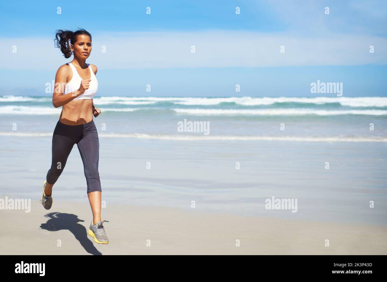 Mid-morning jog to clear her head. Full length shot of a young woman running along the seashore. Stock Photo