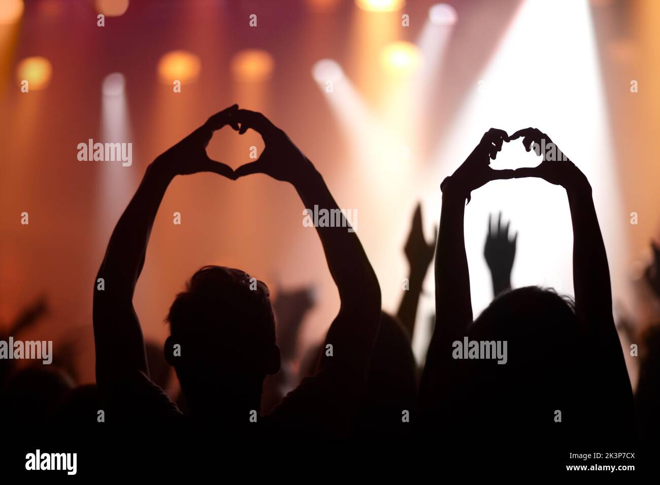 Music lovers. Rearview of audience members at a music concert holding up their hands in a heart symbol. Stock Photo