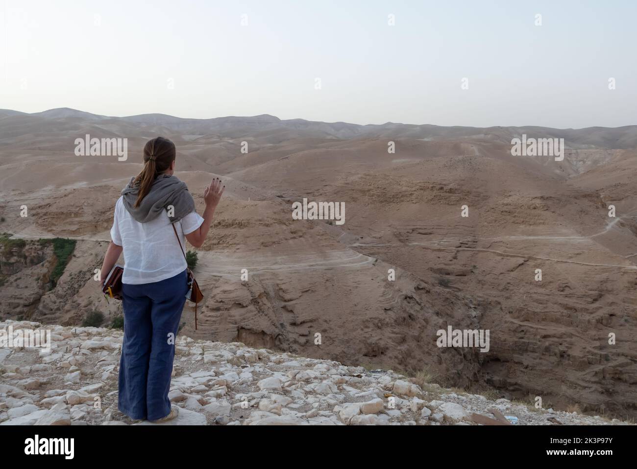 A Christian pilgrim prays as she stands on a cliff above the valley of the Wadi Qelt, located in the Judaean or Judean desert in Israel Stock Photo