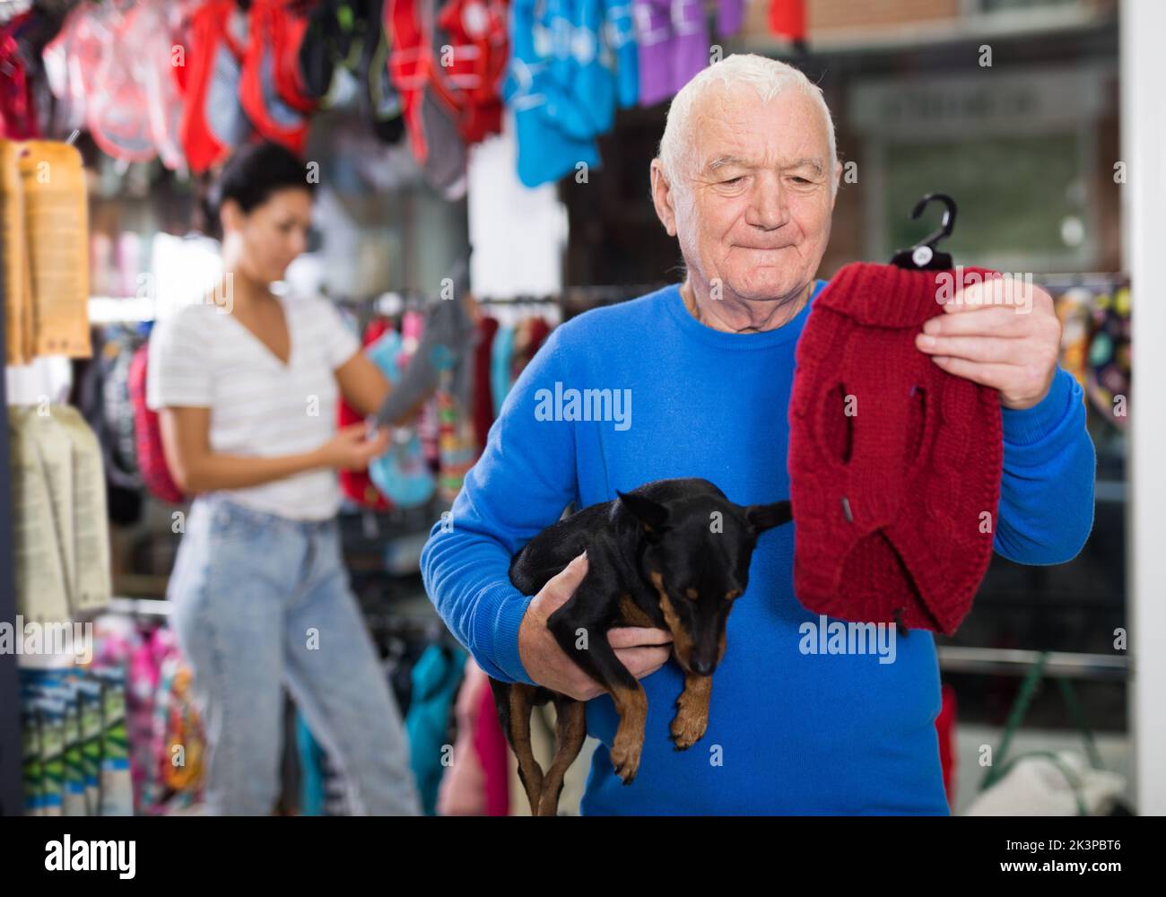 Senior man choosing winter clothes for his dog at pet shop Stock Photo