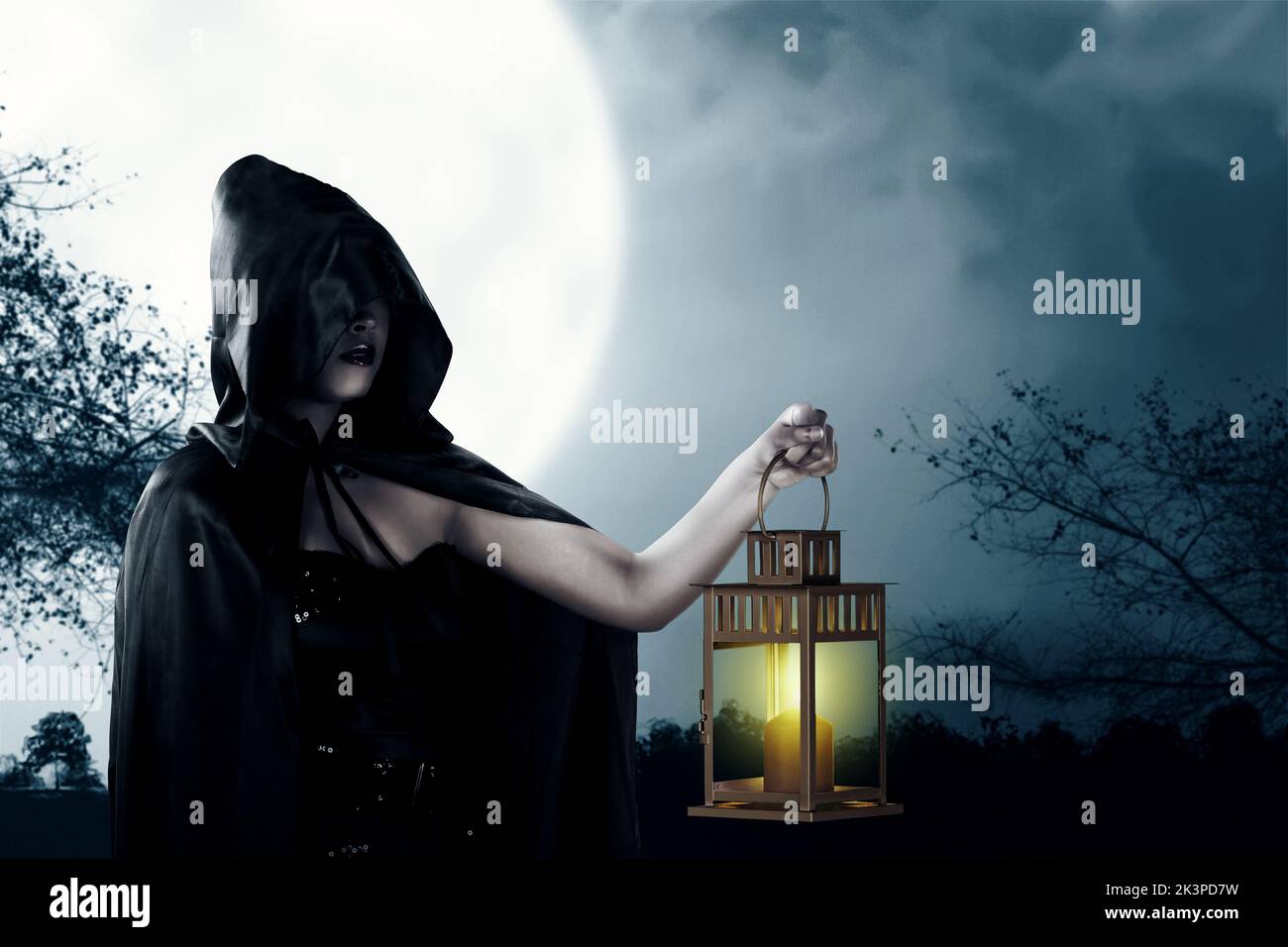 Asian witch woman with a black cloak holding a lantern standing with the night scene background Stock Photo
