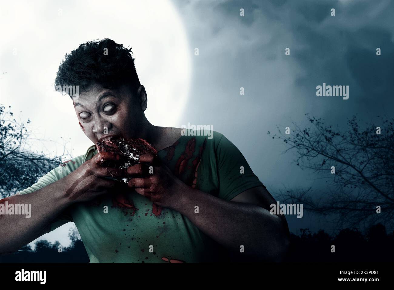 A scary zombie with blood and wound on his body eat the raw meat with the night scene background Stock Photo