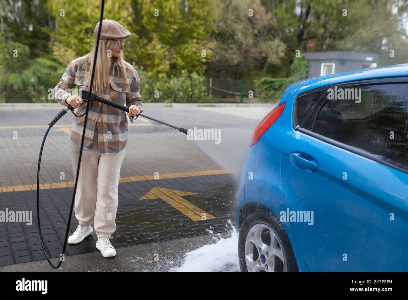 Woman washing a car in a selfservice car wash station with wahing foam