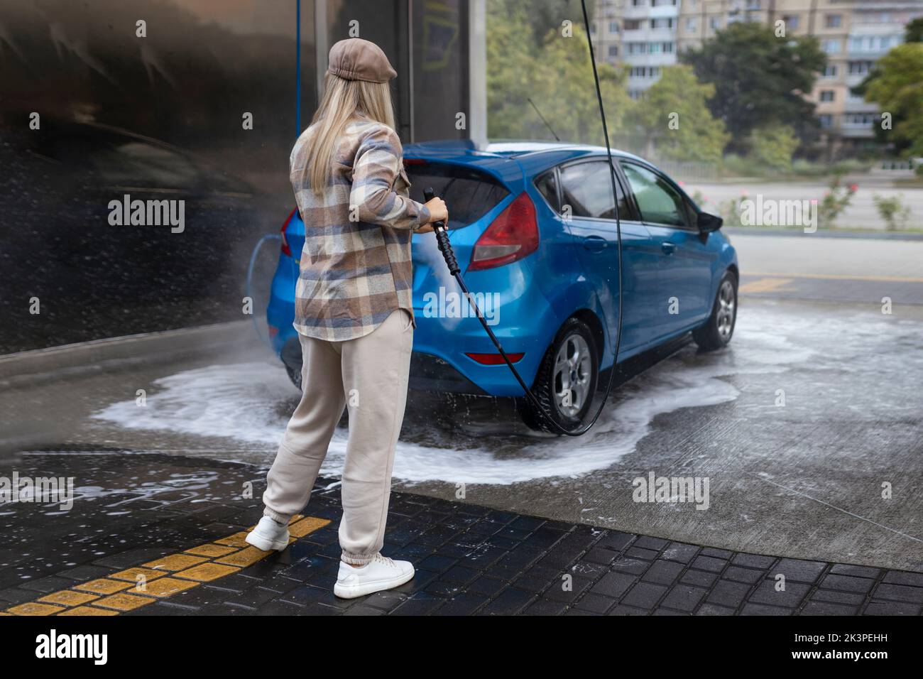 Woman washing a car in a selfservice car wash station with wahing foam