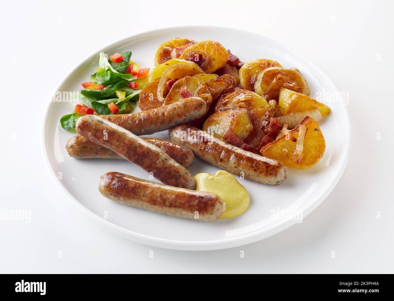From above delicious bratwurst and bratkartoffeln served with sauce and spinach salad on plate on white background Stock Photo