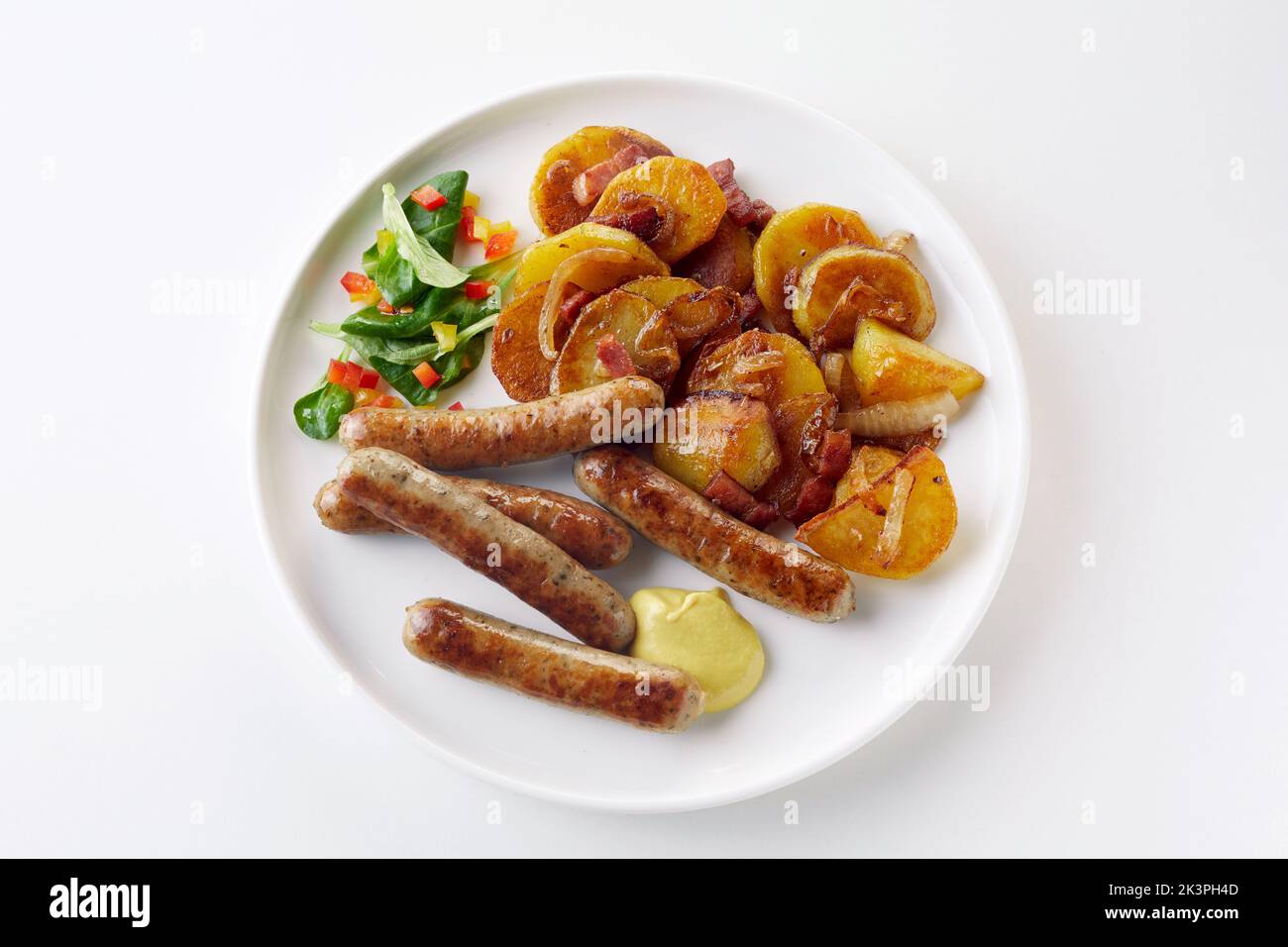 Top view of yummy German bratkartoffeln and bratwurst served for lunch with vegetable salad and mustard sauce on plate on white background Stock Photo