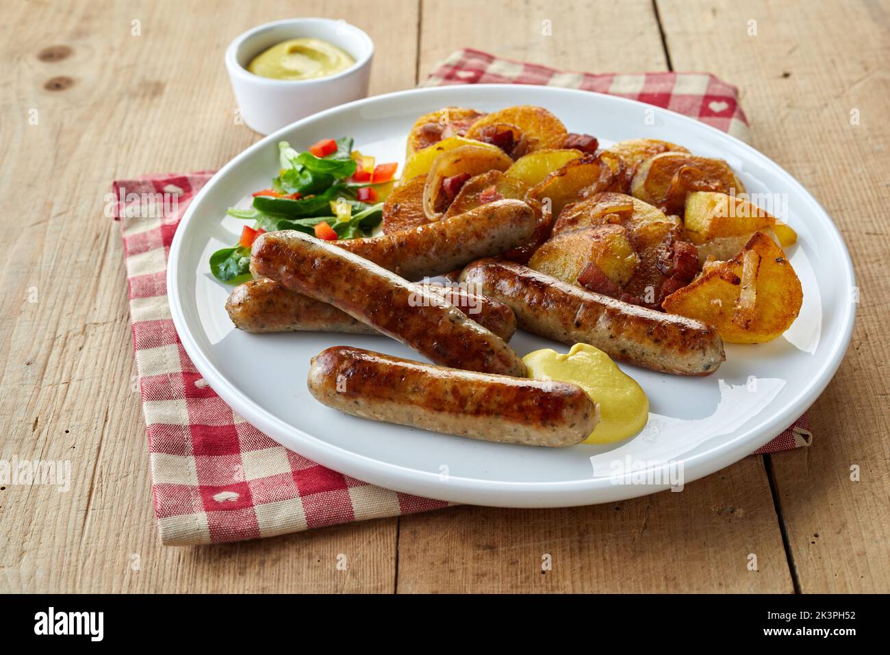 Plate of fried German sausages and potatoes with vegetable salad and mustard sauce placed on