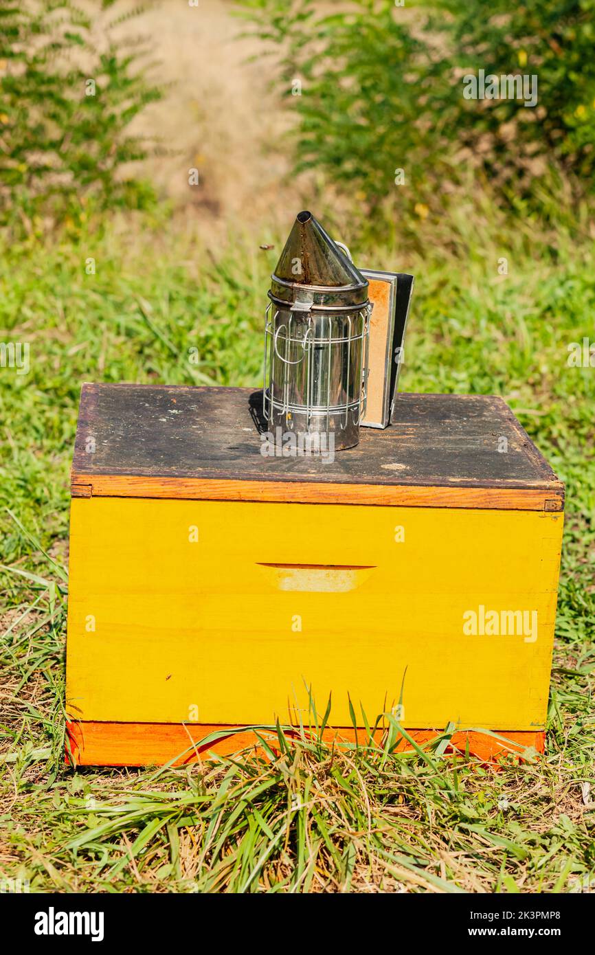 Chrome beekeeper smoker on a one yellow bee hive in the grass field