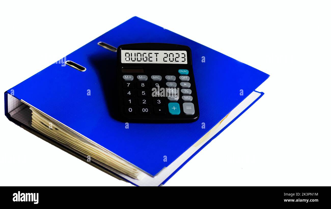 BUDGET 2023 text on the display of a calculator that lies on a blue folder and a white background Stock Photo