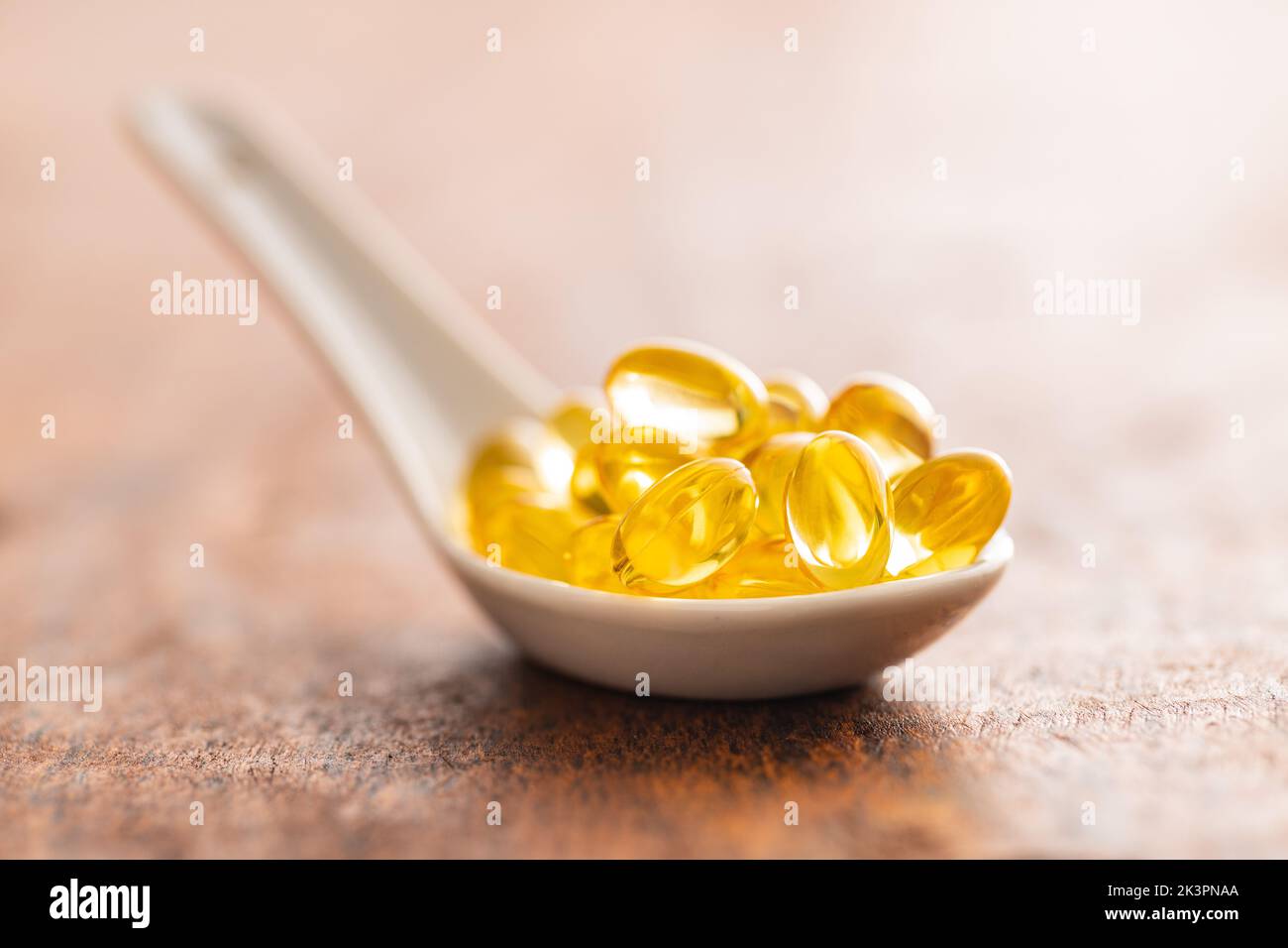 Fish oil capsules. Yellow omega 3 pills in ceramic spoon on the wooden table. Stock Photo