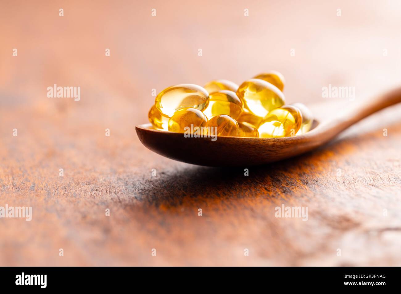 Fish oil capsules. Yellow omega 3 pills in spoon on the wooden table. Stock Photo