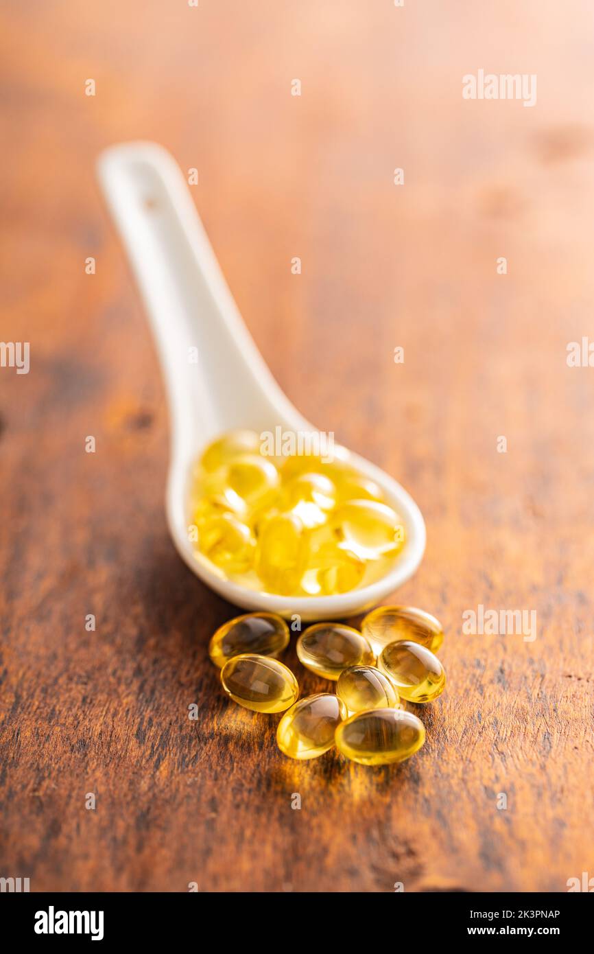 Fish oil capsules. Yellow omega 3 pills in ceramic spoon on the wooden table. Stock Photo