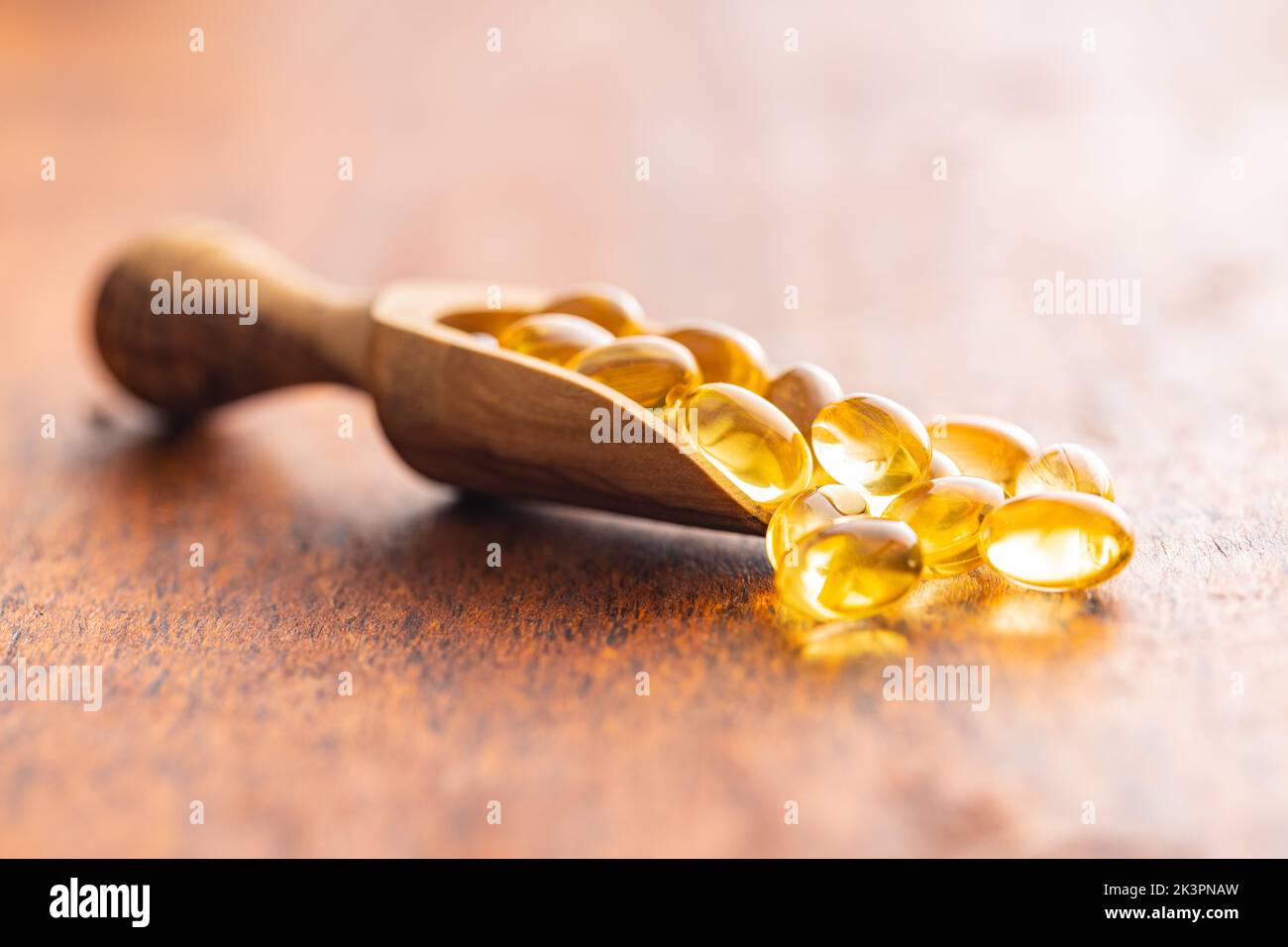 Fish oil capsules. Yellow omega 3 pills in wooden scoop on the wooden table. Stock Photo