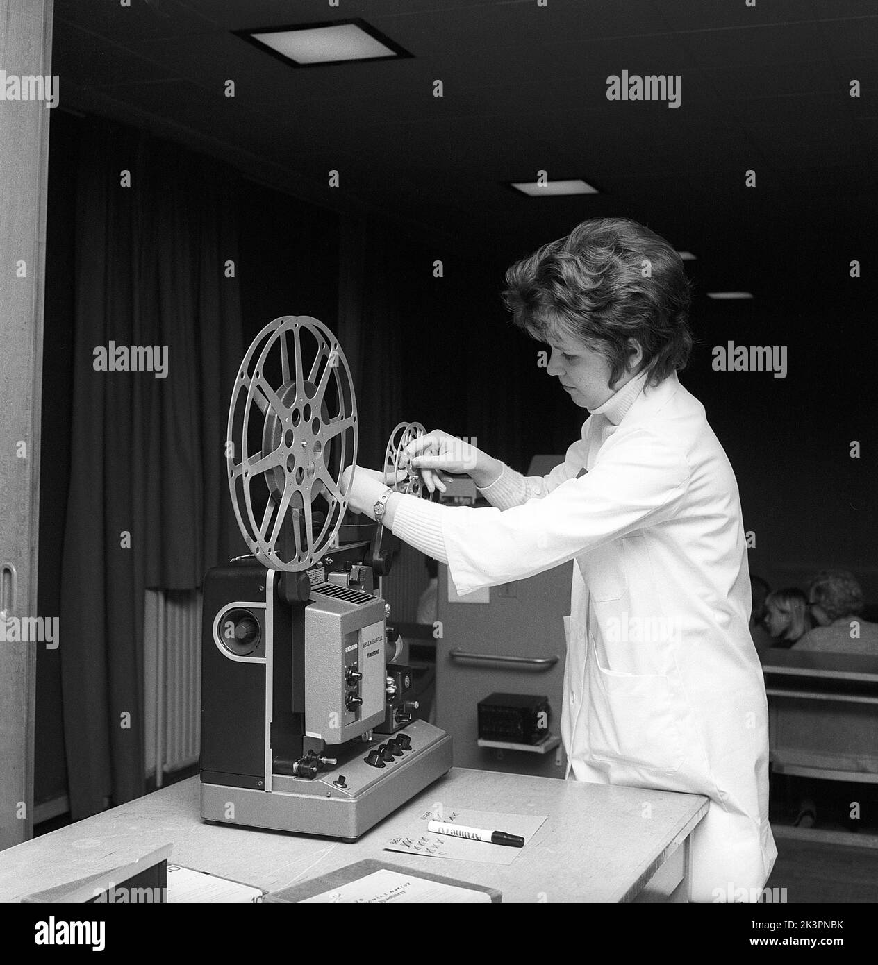 In the 1960s. A young female teacher with a film projector, mounting the film roll. Sometimes short films were shown in the classroom or in a special viewing room, not only for educational puroposes but for entertainment. The film had sound. Once the film roll was viewed, the film was rolled onto a reciever roll and needed to be winded back. Sweden 1968 ref CV77 Stock Photo