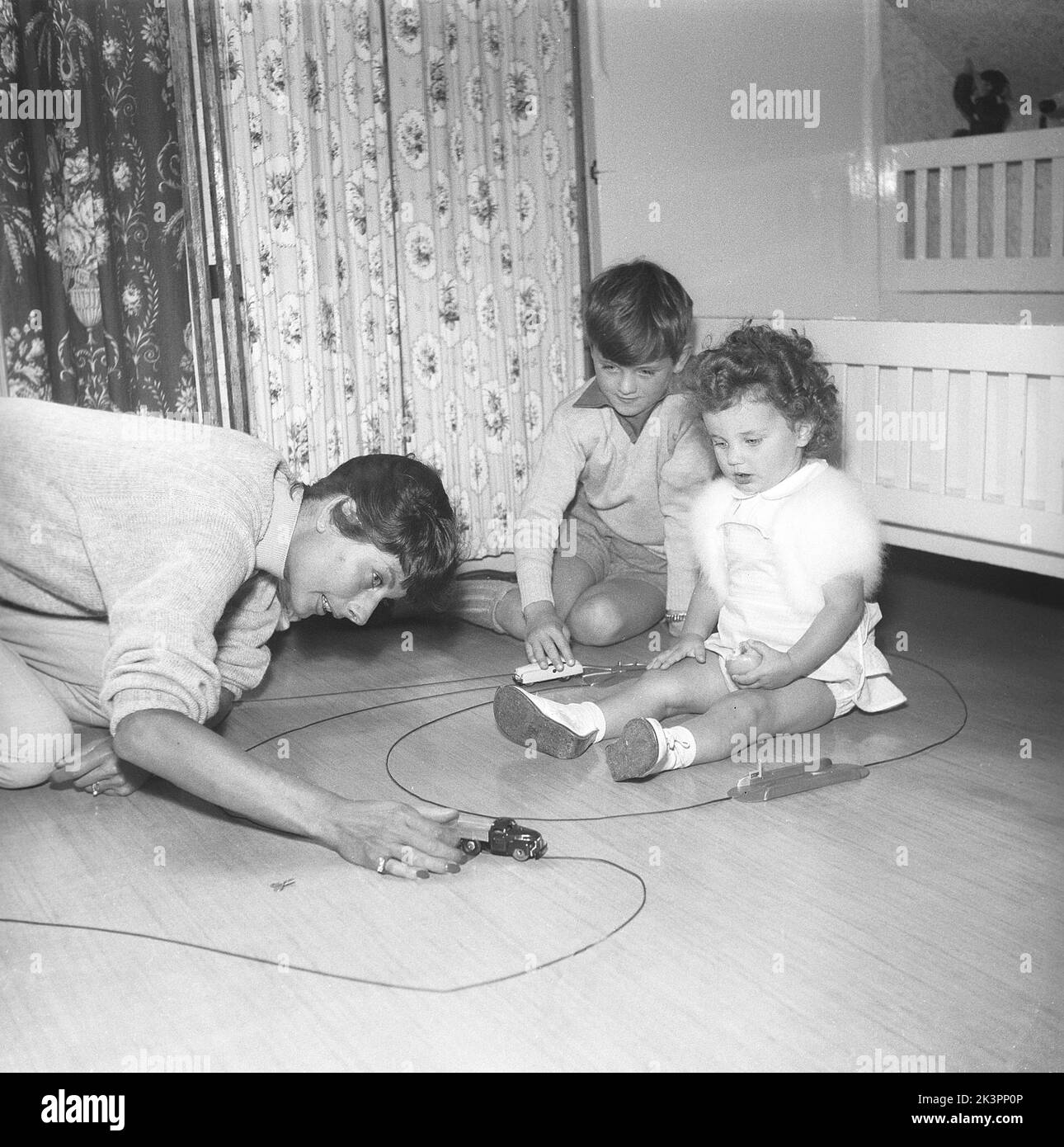 Mother in the 1950s. Mrs Erica Sundt with her two children playing with toys on the floor. A typical simple toy of the 1950s where the winded up cars ran along a track, in this case a flexible metal track. The key that was used to wind the toys up is visible on the floor beside her hand.   Sweden 1954 Kristoffersson ref BX24-4 Stock Photo