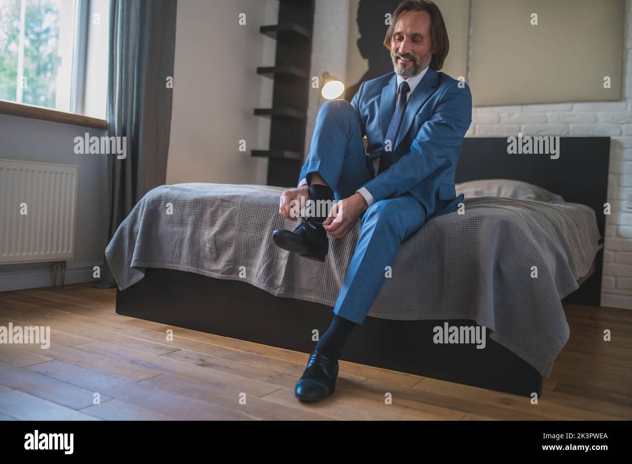 Man in blue suit putting on his shoes wile sitting on the sofa Stock Photo