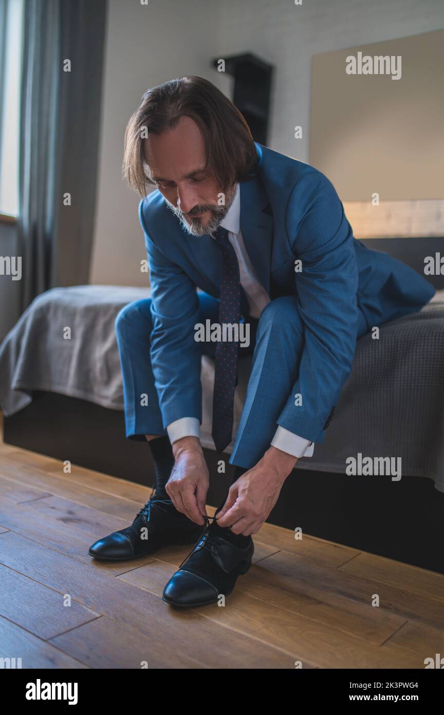 Man in blue suit putting on his shoes wile sitting on the sofa Stock Photo