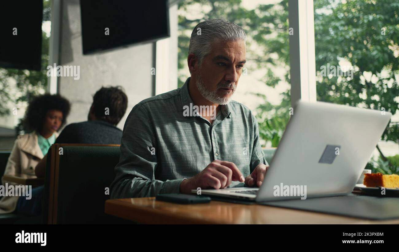Older executive opening laptop seated at cafe store working remotely ...
