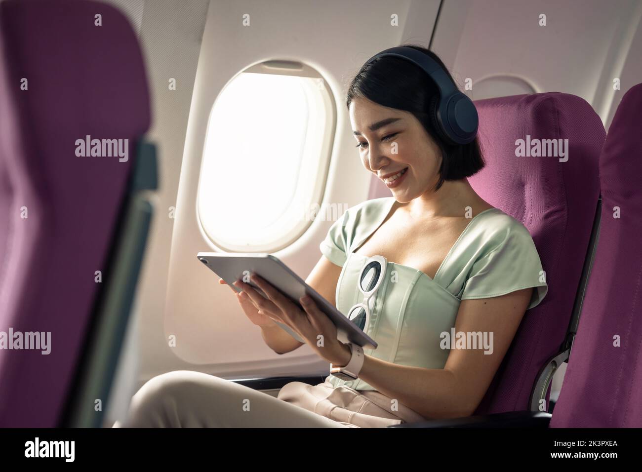 Passenger using tablet computer in airplane cabin during flight. watching series. Stock Photo