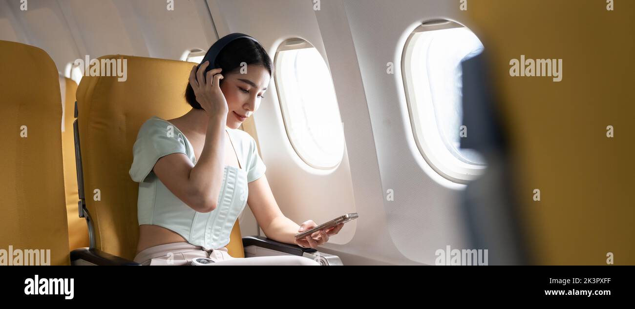 Young woman with mobile phone and headphones listening to music in airplane during flight Stock Photo