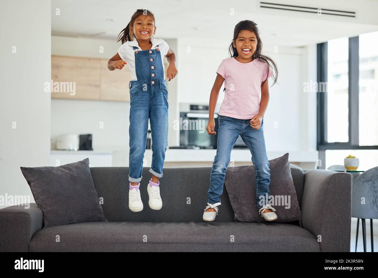 Excited girl kids jumping on living room sofa furniture at home for fun, energy and play games. Portrait crazy, happy and wild young children adhd Stock Photo