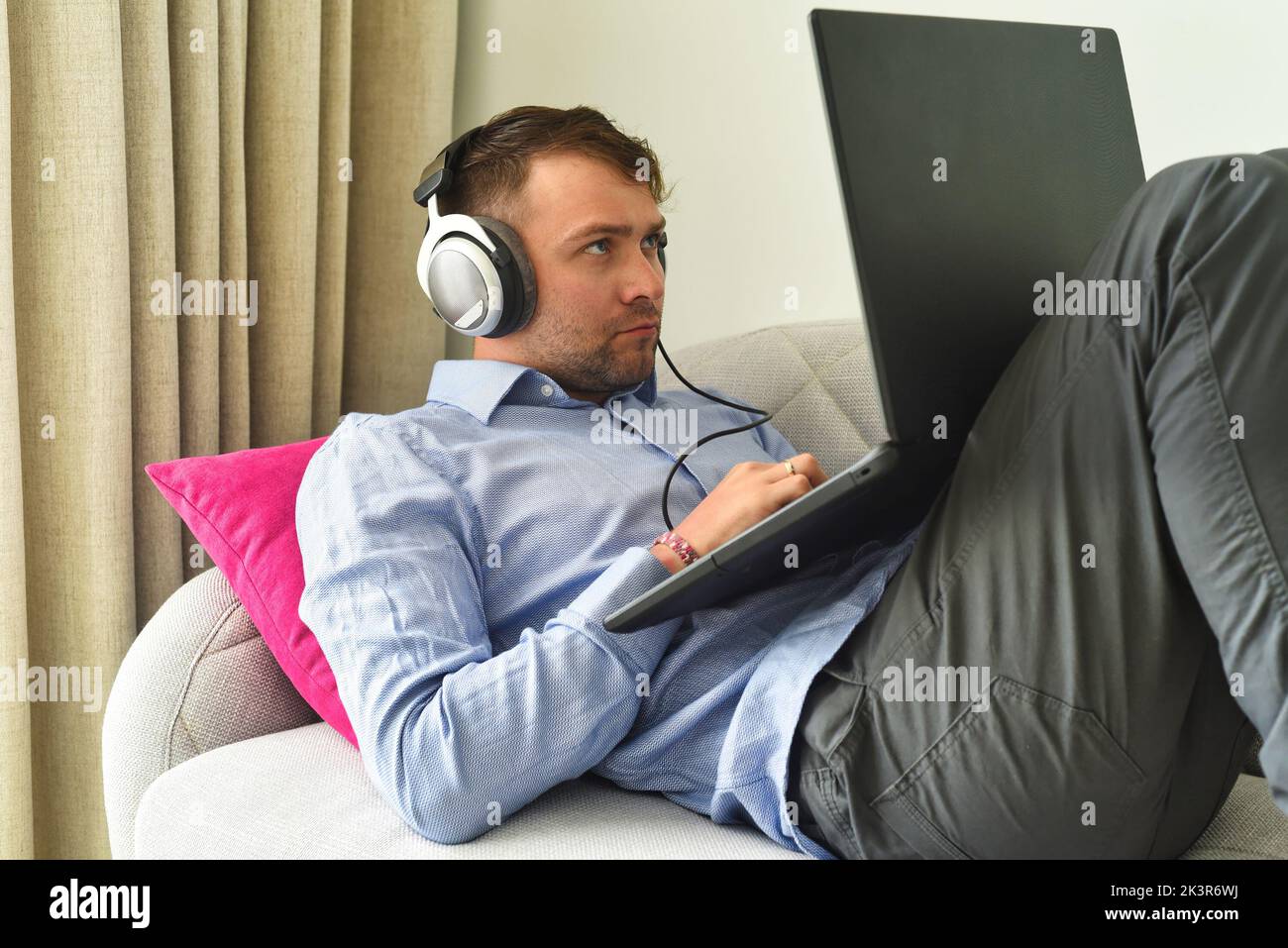 Young man beat maker working from home with his laptop laying on couch