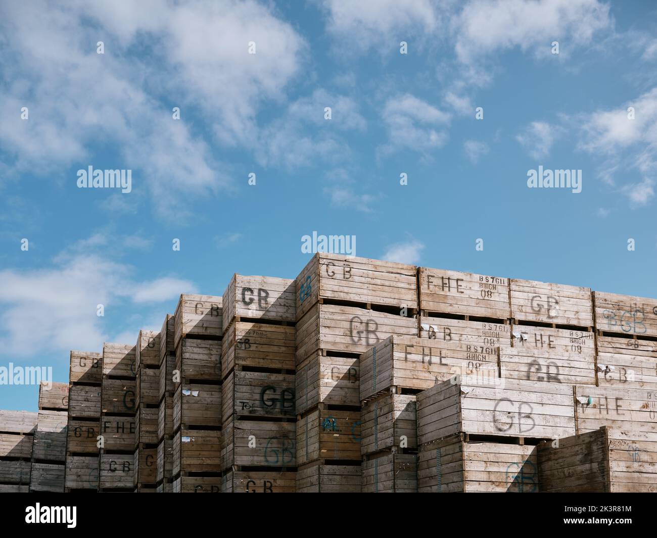 Wooden farm crates with GB identity markings stacked against a blue sky. Stock Photo