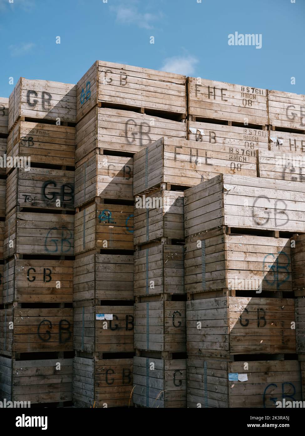 Wooden farm crates with GB identity markings stacked against a blue sky. Stock Photo