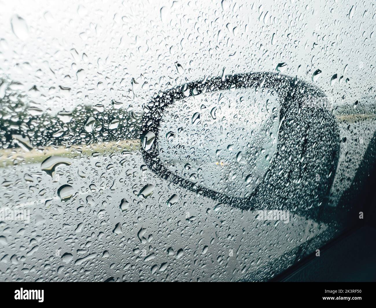 Car wing mirror and side window covered in raindrops during summer ...