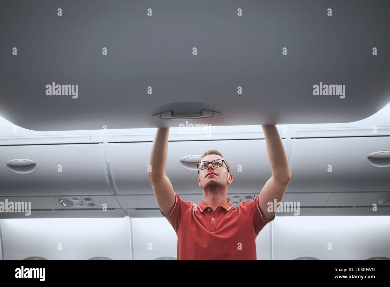 Man travel by airplane. Passenger putting hand baggage in lockers above seats of plane. Stock Photo